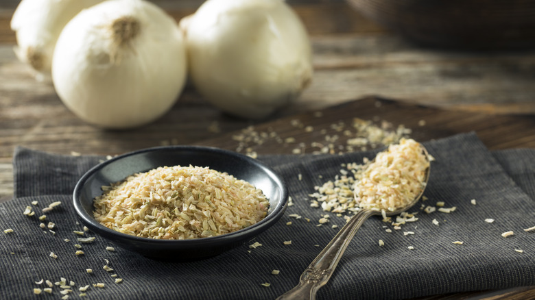 White minced dried onions in a bowl on cloth in front of fresh bulbs