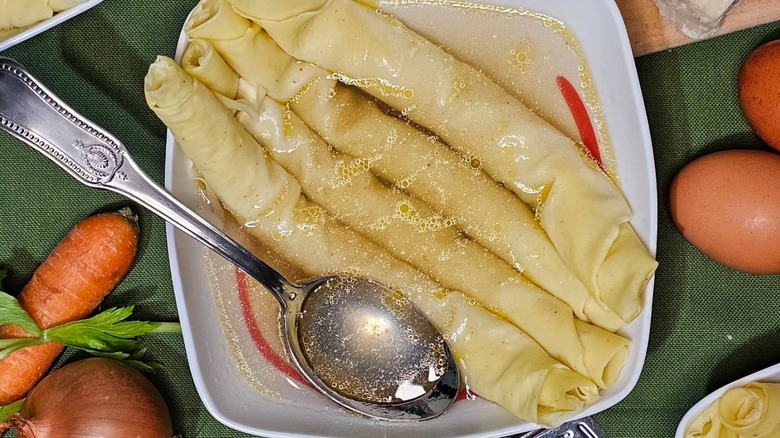 A bowl of scrippelle 'mbusse sits on a table surrounded by vegetables and eggs.