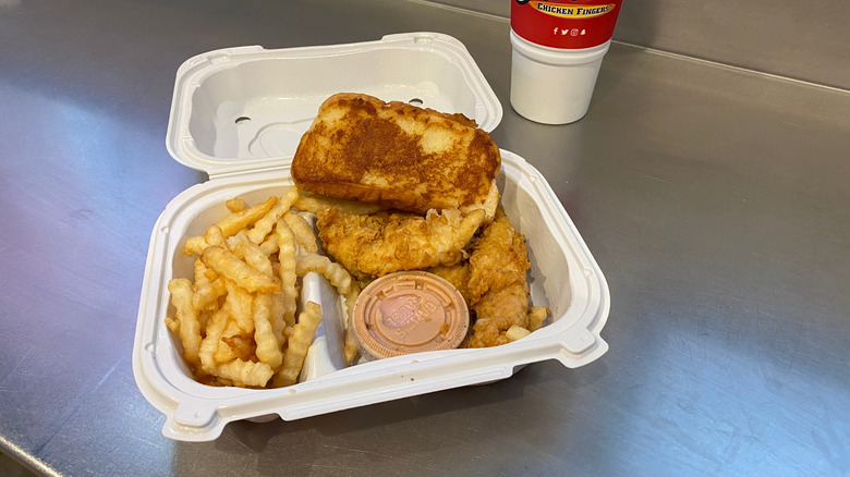 A Raising Canes combo meal featuring chicken and fries with its sauce in a plastic box on a flat surface