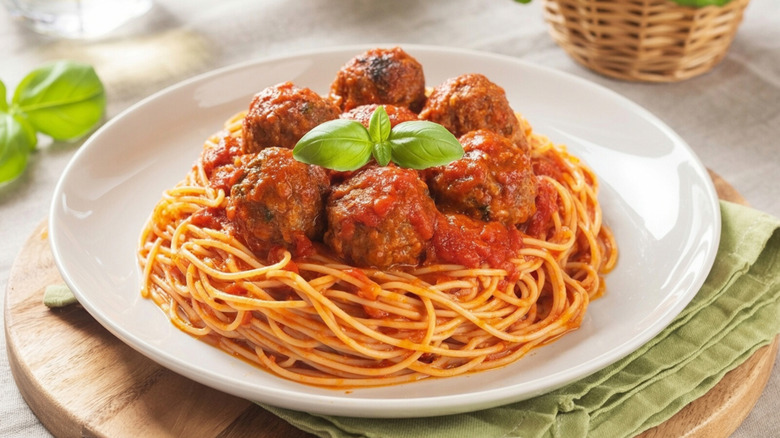 Spaghetti and meatballs neatly served on a white plate with basil garnish.