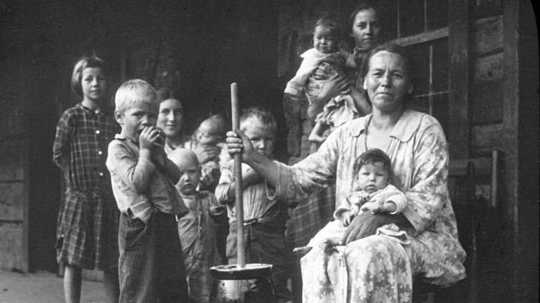 A historical image of a family in West Virginia, the matriarch holding the handle of a butter churner