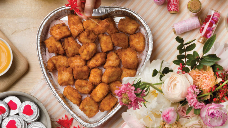 A heart-shaped tray full of chicken nuggets on a table next to some Valentine's decorations and flowers