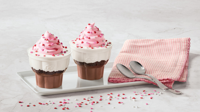 Two small ice cream cupcakes on a white tray with a napkin and spoons next to it
