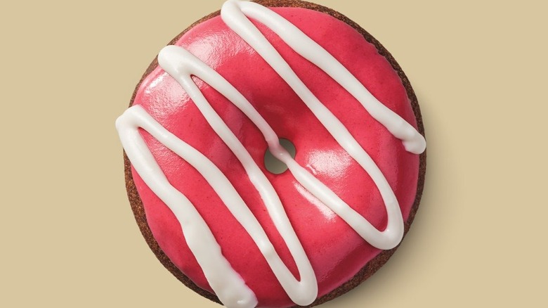 A chocolate cake donut covered with raspberry icing with vanilla drizzle