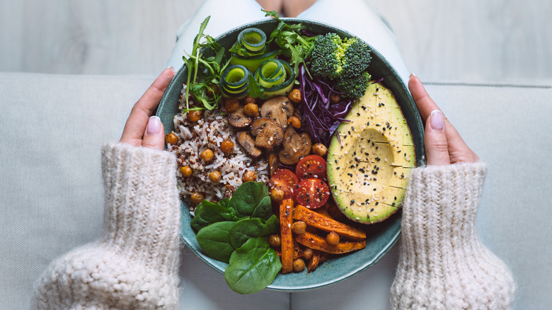 Hands holding bowl of vegetables, rice, and chickpeas