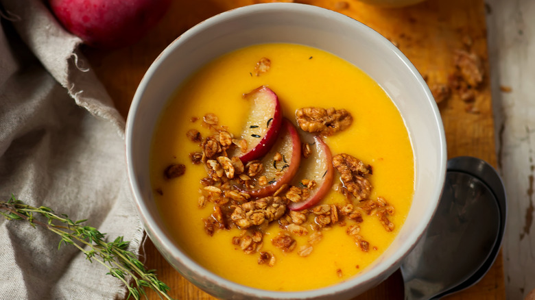 A bowl of butternut squash and apple soup with sliced apples on top