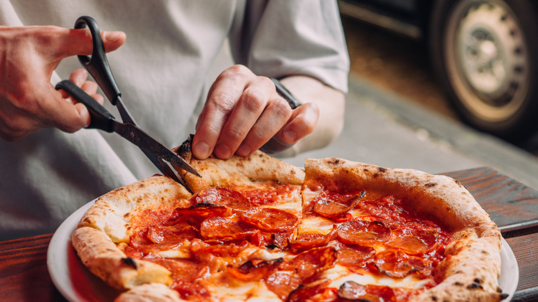 hands using scissors to cut pepperoni pizza
