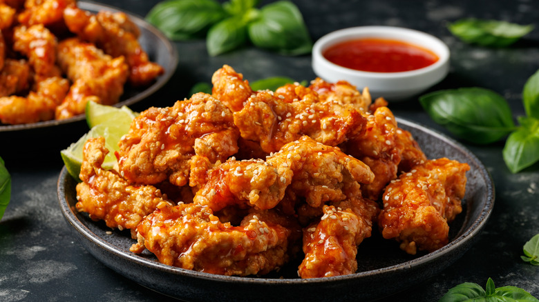 Korean fried chicken with a red dipping sauce, lime slices, and basil leaves