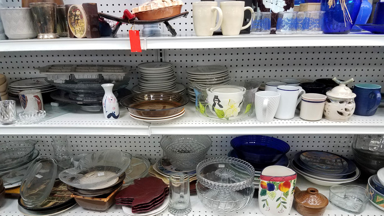 Shelves at a thrift store stuffed with glassware such as pots, wine glasses, and mugs