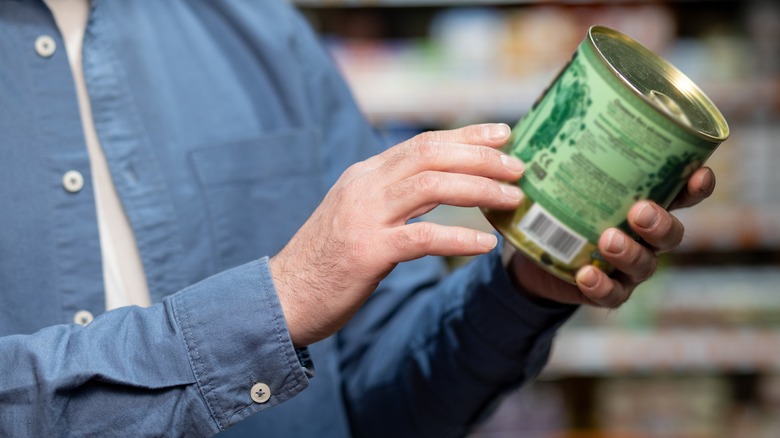 Someone in a grocery store aisle holding a green can of food