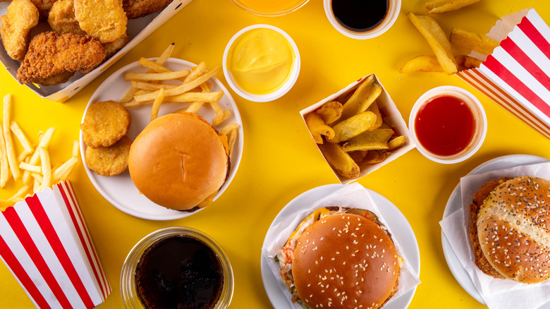 Various fast food options on a yellow background, including burgers, fries, and chicken nuggets