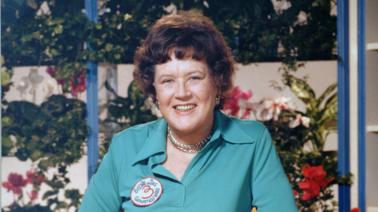 Julia Child stands and smiles at the camera.