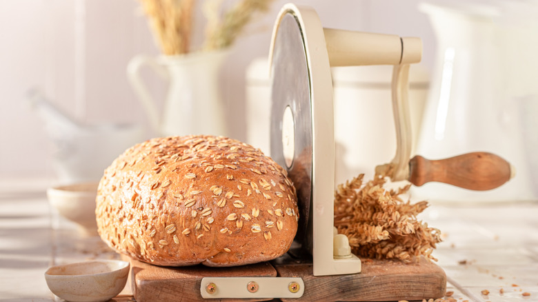 A loaf of bread topped with oats placed on a manual bread slicer