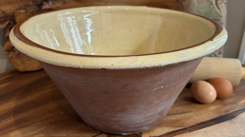 A vintage French pancheon displayed on a table next to eggs and a rolling pin