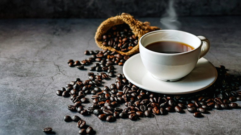 A white mug of coffee among coffee beans and a bag of beans