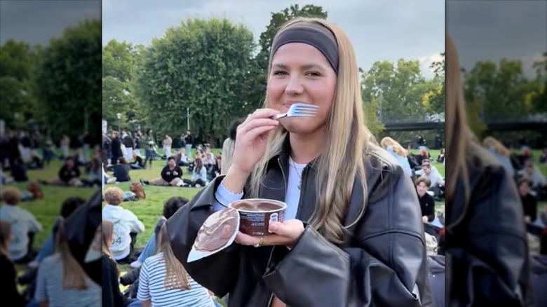woman eating pudding with fork in park with crowd