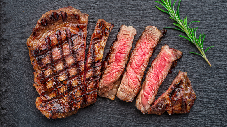 a sliced grilled ribeye steak on a slate board with a sprig of rosemary beside it