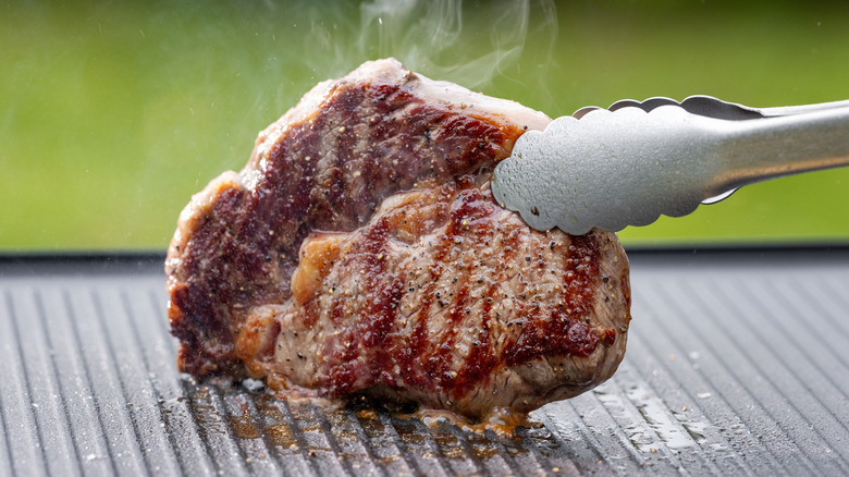 tongs holding a grilled ribeye and searing the edges on a hot grill
