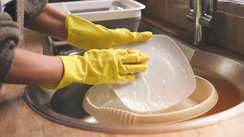 Washing dishes in plastic tub in sink