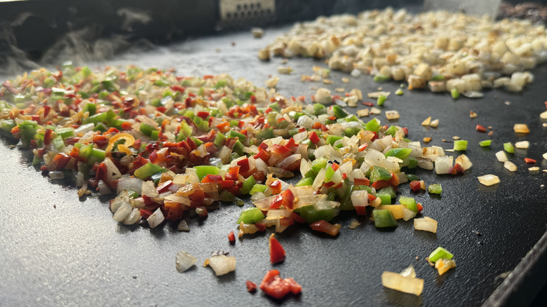 Mixture of diced peppers and onions cooking on a griddle