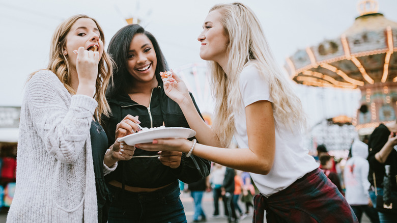 Three people sharing a plate with blurred carnival background.