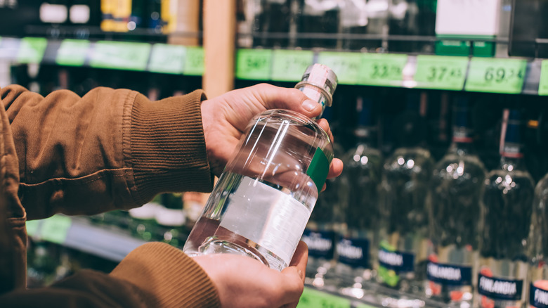male shopper holds up bottle of vodka in liquor aisle