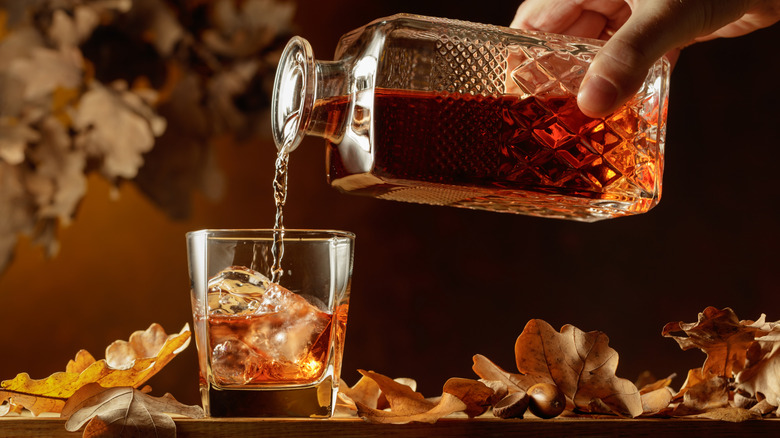 bourbon pouring from a decanter into a glass surrounded by autumn leaves