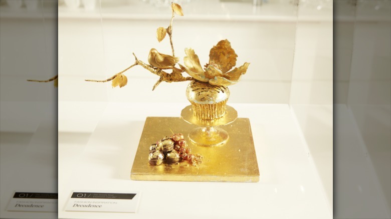 World's most expensive cupcake on display on gold tray, topped with giant gold flower.