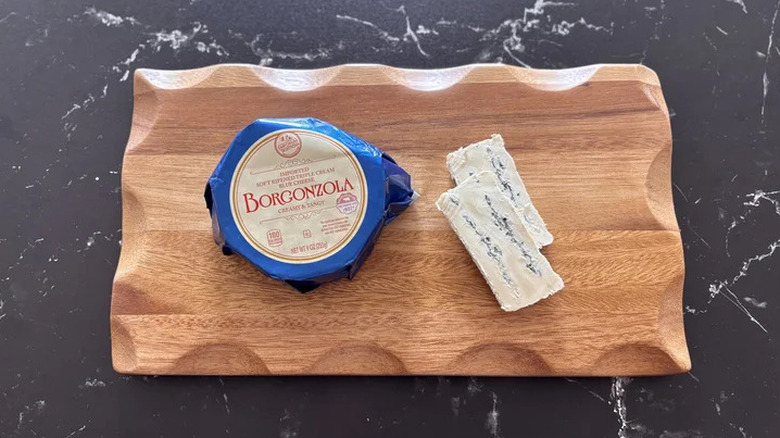 A round of Aldi's borgonzola cheese on a wooden cutting board beside two slices of the cheese
