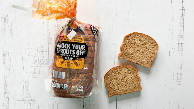 Loaf of Simply Nature Knock Your Sprouts Off Bread next to two slices of bread on white surface