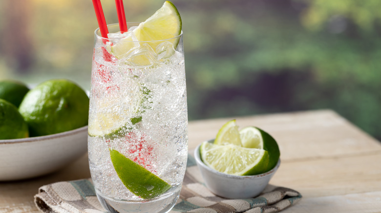 Glass of sparkling water with red straws and lime wedge