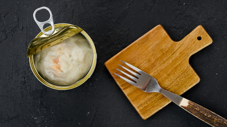 an open can of crab meat with wood board