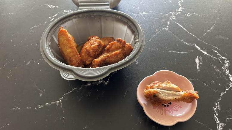 A container of Pizza Hut's Garlic Parm wings beside a half-eaten wing in a small, pink bowl
