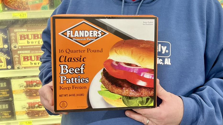 A person in a grocery store holding a box of Flanders Classic Beef Patties