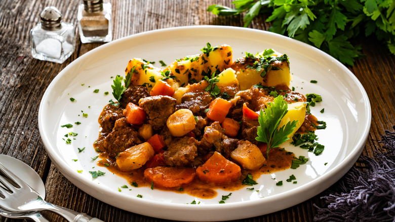 Plate of scratch-made pot roast and vegetables next to cutlery, herbs, and seasonings