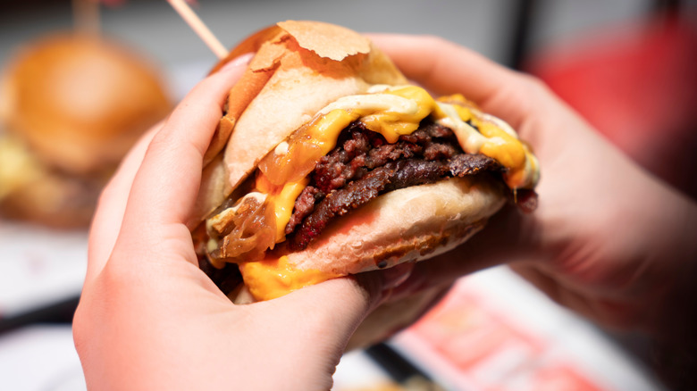 Hands holding a smash burger with cheese.