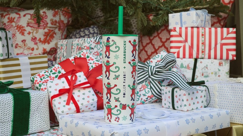Starbucks in roller rabbit branded tumbler covered in green monkeys in red pajamas on top of some Christmas presents