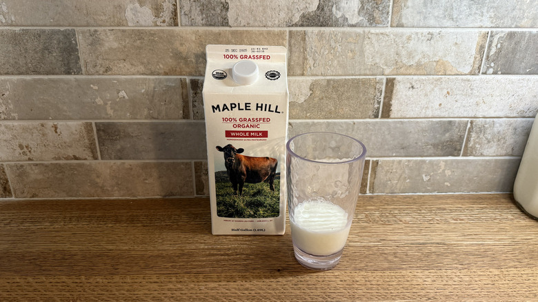 A carton of Maple Hill 100% Grassfed Organic Whole Milk on a counter next to a glass of milk