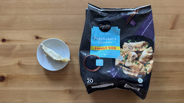 one cooked potsticker in a small dish beside a bag of Signature Select Chicken Potstickers