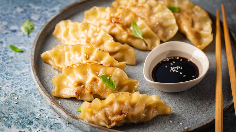 a plate of potstickers garnished with sesame seeds beside a dish of dipping sauce and chopsticks
