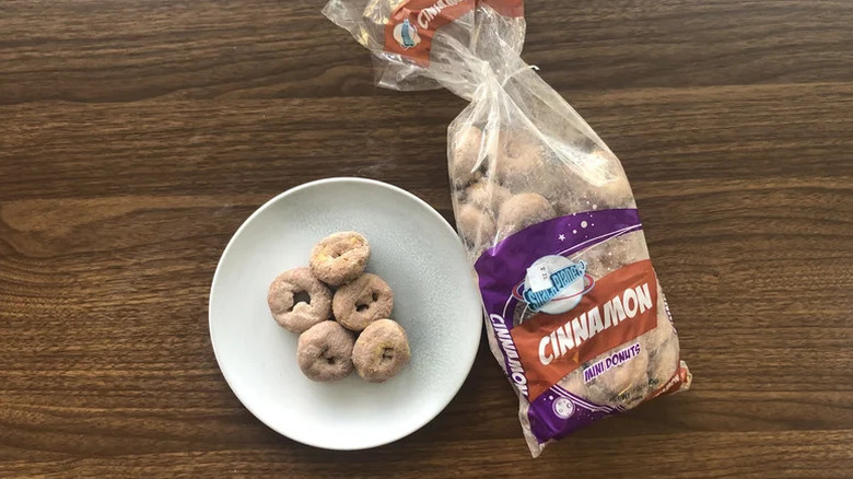 The plastic bag of snack Planet mini cinnamon donuts on a wooden table next to a white plate holding five Donuts
