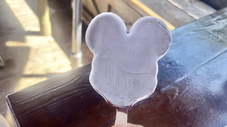 Hand holding Mickey's ice cream bar over a wooden tabletop