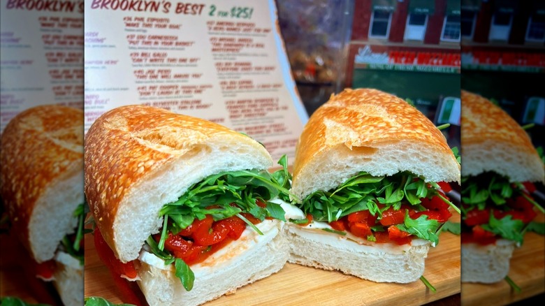 Hero with mozzarella, arugula, and red peppers with a menu in the background