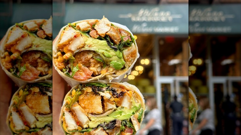Hand holding a chicken wrap up in front of the Milano Market storefront
