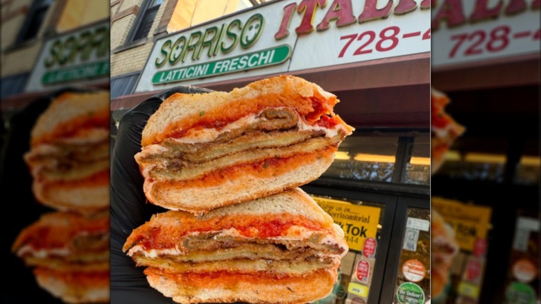 Fried eggplant and mozzarella sub held in front of the Sorriso Italian Salumeria storefront