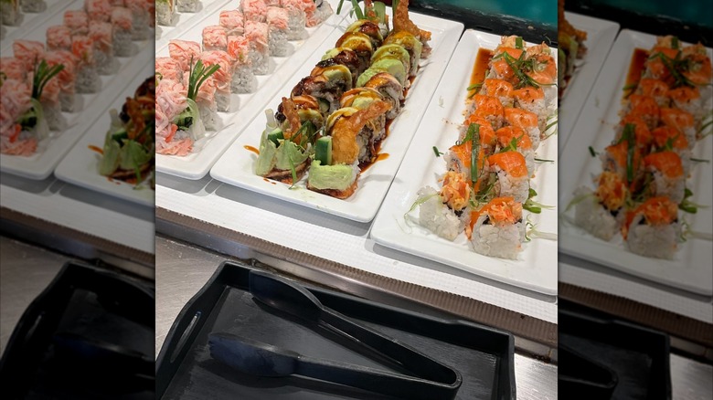 Three trays of assorted sushi rolls with tongs