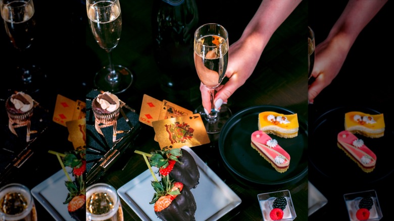 Hand holding glass of champagne with chocolate-dipped strawberries and cakes on small plates