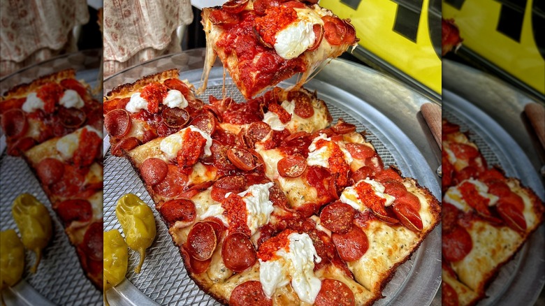 Person picking up a slice of Detroit-style pizza from a full pie