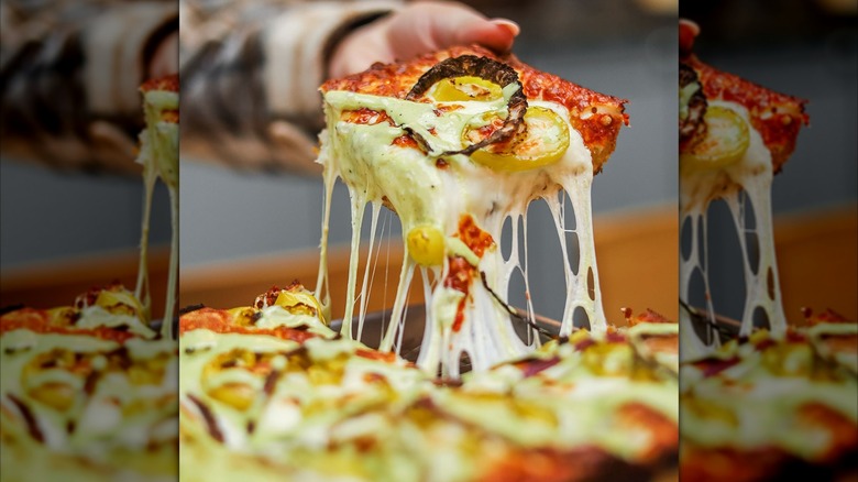 Hand picking up a slice of pizza with cheese stretching