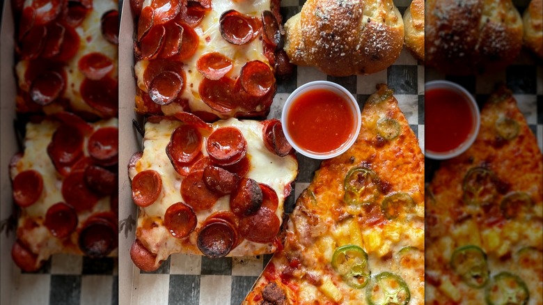 Slices of Detroit-style pizza in a box with sauce, garlic knots, and a thin-crust slice